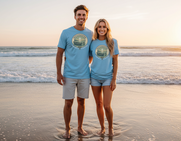 Man and woman standing on a beach wearing matching blue t-shirts with a logo.